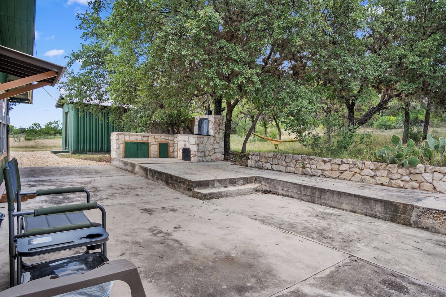 An outdoor patio area with a stone wall, a hammock, and a green chair.