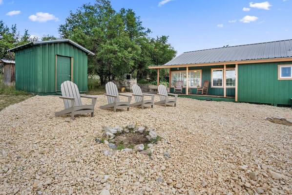 A building with a green exterior, a gravel patio, and four Adirondack chairs.