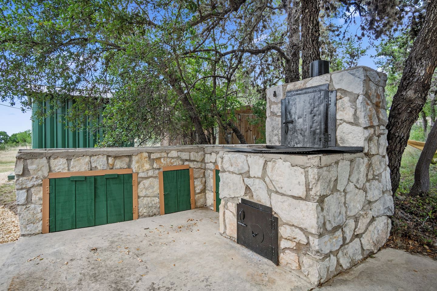 Une structure extérieure en pierre dotée d’un barbecue intégré, de portes vertes et d’un mur en pierre.
