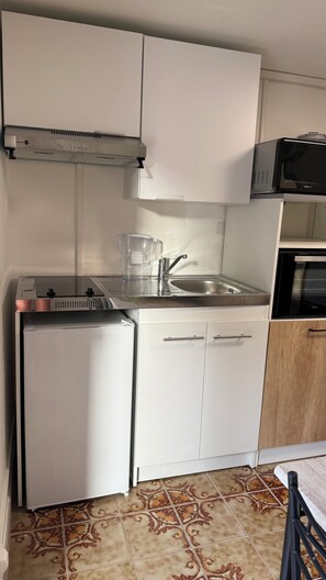Une cuisine compacte avec des meubles blancs, un évier en acier inoxydable, un four à micro-ondes et un petit réfrigérateur.