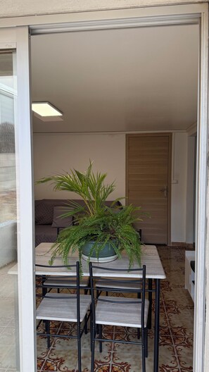 Un espace de vie et de salle à manger à aire ouverte comprenant une table à manger, des chaises, une fougère en pot, un canapé et une porte coulissante.