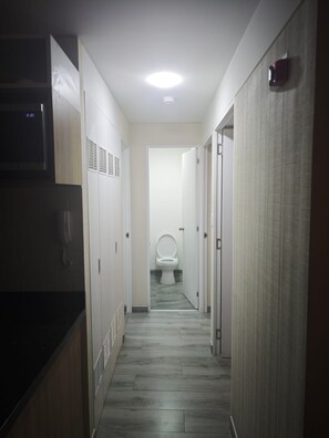 Ein schmaler Flur mit einer Toilette am Ende, einer Mikrowelle links und einem Rauchmelder rechts.
