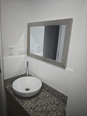 Een badkamer met een wit wastafel, een granieten aanrechtblad en een spiegel met een reliëf lijst.