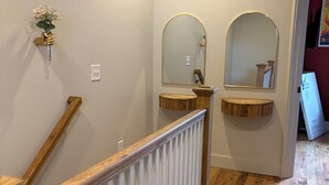 Una escalera con barandillas de madera y un pasamanos blanco que conduce a una habitación con piso de madera y un espejo colgado en la pared.