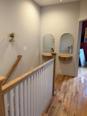 A staircase with wooden handrails and a white railing, leading to a room with a wooden floor and a wall-mounted mirror. - Howdy Haven - Come stay in vibrant Nashville. House just updated! (Nashville)
