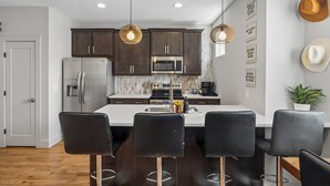 Una cocina moderna con armarios oscuros, electrodomésticos de acero inoxidable y una isla central con taburetes de bar.