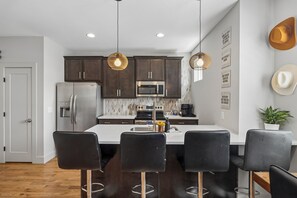 A modern kitchen with dark cabinets, stainless steel appliances, and a central island with bar stools. - Howdy Haven - Come stay in vibrant Nashville. House just updated! (Nashville)