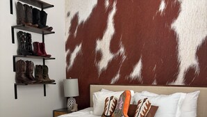 Un dormitorio con colcha a cuadros, cabecera estampada con motivo de piel de vaca y estante con botas.