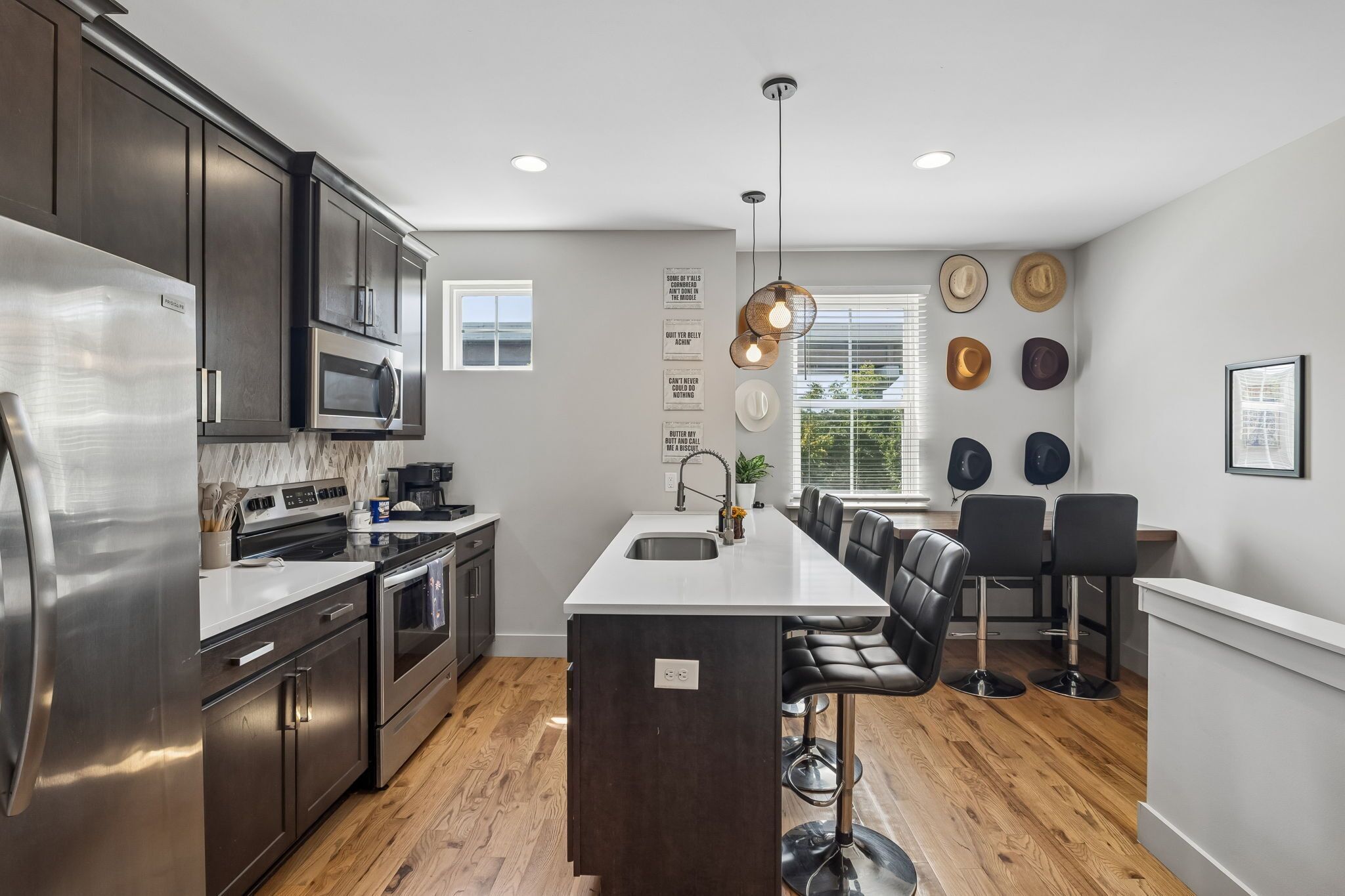 A modern kitchen with stainless steel appliances, a central island with bar stools, and a dining area with a large window.