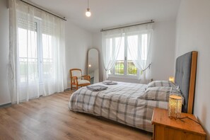 A bedroom with a bed, a chair, a bedside table with a lamp, and a window with curtains. - Le Gîte de la Vanne - Saint-Benoît-sur-Vanne (SAINT BENOIST SUR VANNE)