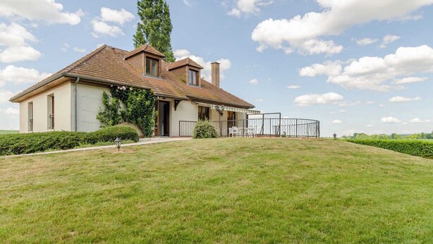 Ein zweistöckiges Haus mit geneigtem Dach, einem eingezäunten Garten und blauem Himmel.