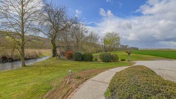 A riverside pathway with a lamp post, a grassy area, and a hedge.