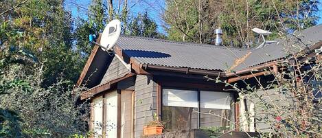 A rustic cabin with a sloped roof, surrounded by dense foliage and trees.