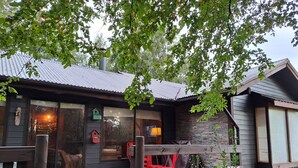 Mökki, jossa on puinen terassi, suuret ikkunat ja kivestä tehty ulkoseinä.