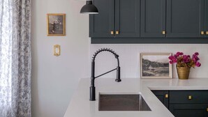 Una cocina con armarios oscuros, una encimera blanca, un grifo negro y una lámpara colgante.