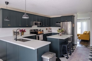 A modern kitchen with dark cabinets, white countertops, stainless steel appliances, and pendant lighting.