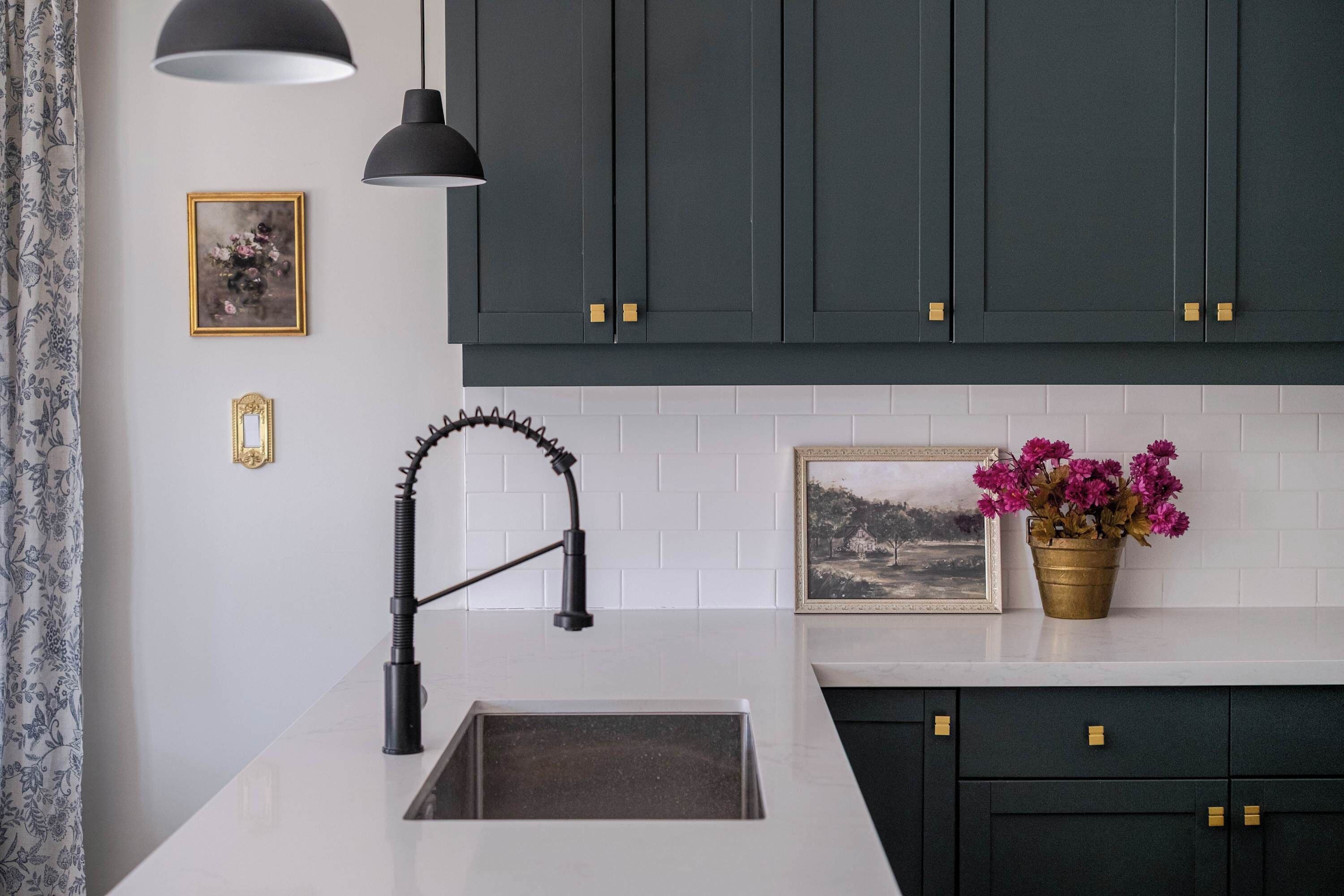 Une cuisine moderne avec des meubles de couleur sombre, un plan de travail blanc, un robinet noir et une plante en pot.