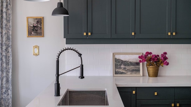 Una cocina moderna con armarios oscuros, una encimera blanca, un grifo negro y una planta en maceta.