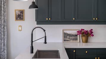 Une cuisine moderne avec des meubles de couleur sombre, un plan de travail blanc, un robinet noir et une plante en pot.
