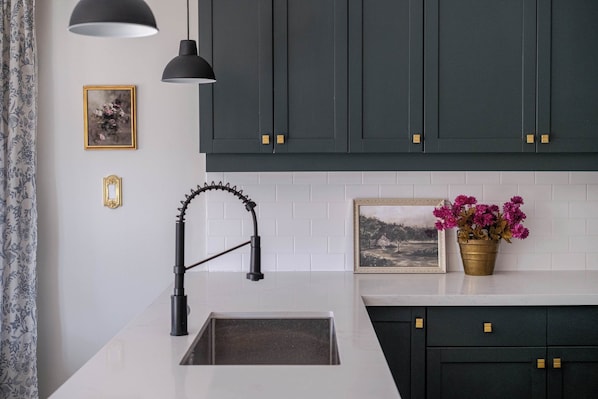 A modern kitchen with dark cabinets, a white countertop, a black faucet, and a potted plant.