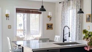 Cocina con una isla central, luces colgantes, una ventana con persianas y apliques de pared.
