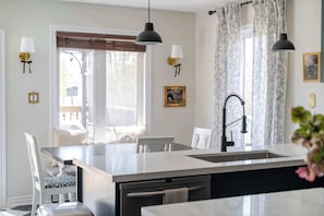 A kitchen with a central island, pendant lights, a window with blinds, and wall-mounted sconces.