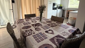 A dining area with a table covered in a patterned tablecloth, surrounded by wicker chairs. A vase with flowers is placed on the table. - A cozy home for relaxing moments, perfect for families or friends (Cuili Murvoni)