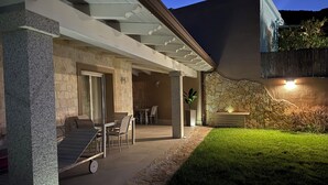 A covered patio area with outdoor furniture, a stone wall, and a grassy lawn. - A cozy home for relaxing moments, perfect for families or friends (Cuili Murvoni)