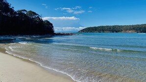 Una platja amb aigua cristal·lina, sorra daurada i un turó boscós al fons.