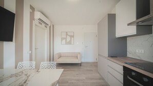 A modern kitchen with a dining area, a sofa, and a TV mounted on the wall. - Sundown Living | New & Modern Apartment | 200 m from the beach | Balcony | Air conditioning (Lignano Sabbiadoro)
