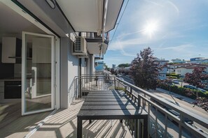 Een balkon met uitzicht op de straat en gebouwen, een schuifglazen deur en een airconditioning.