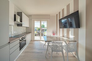 Eine moderne Küche mit Essbereich, einem an der Wand befestigten Fernseher und Blick durch die Glastür.