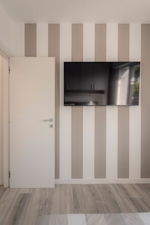 Ein modernes Zimmer mit einem an der Wand mit vertikalen Streifen angebrachten Flachbildfernseher, einer weißen Tür und Holzböden.