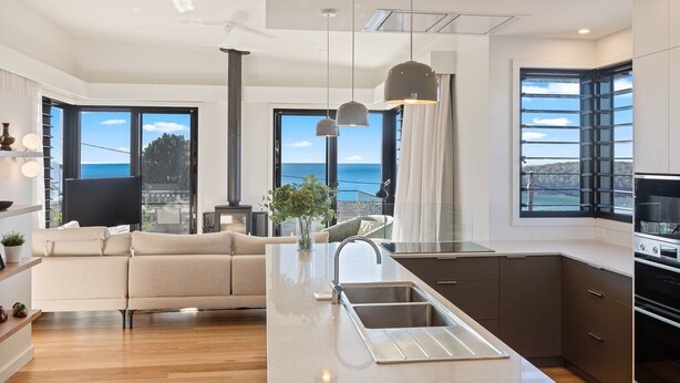Een moderne keuken met een centraal eiland, een zithoek met een bank, en grote ramen met uitzicht op de oceaan.