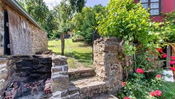 Un edificio de piedra con fachada rústica, una escalera de piedra y un jardín con flores rojas.
