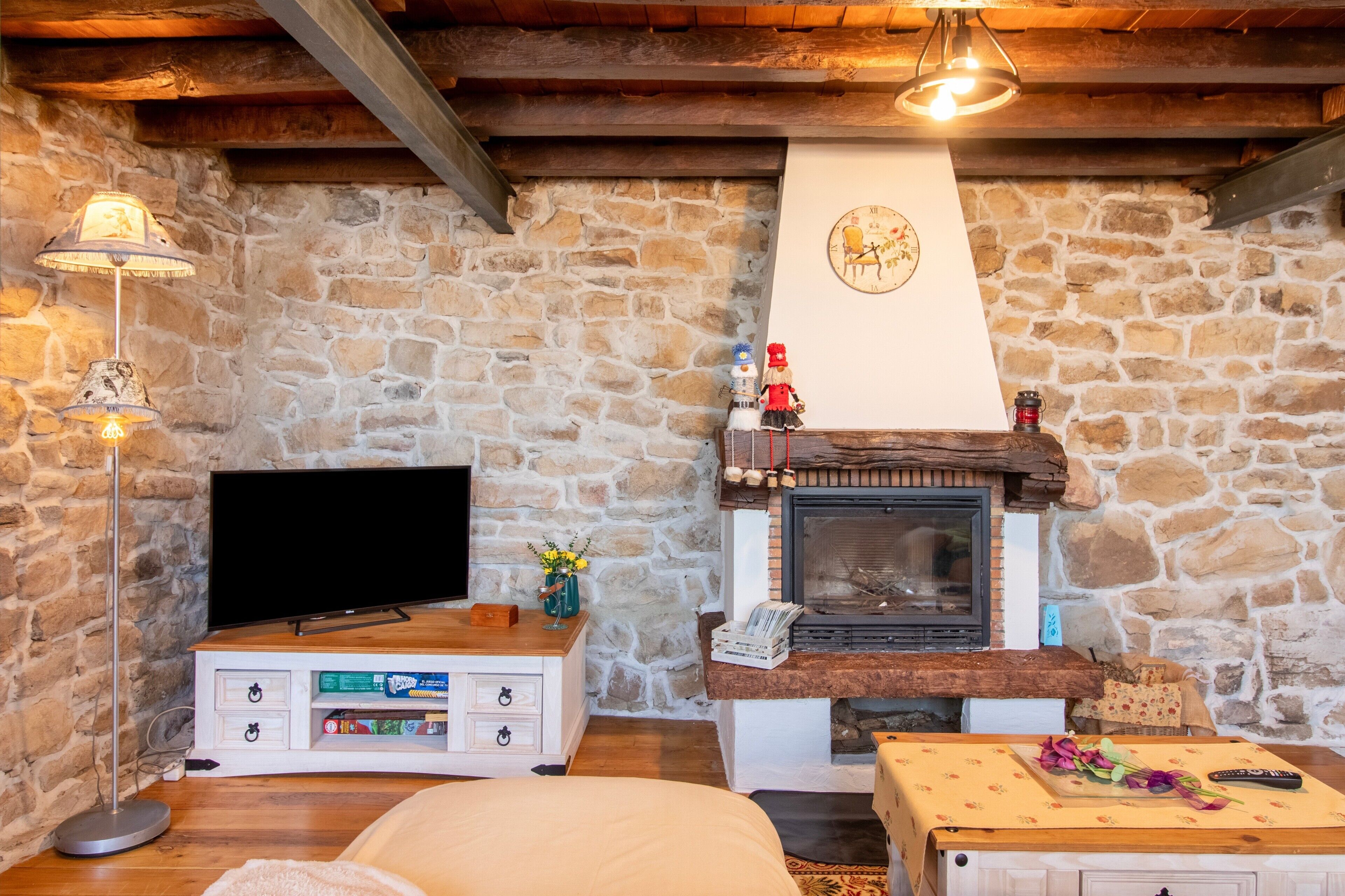 Habitación de paredes de piedra con chimenea, un televisor de pantalla plana, un armario de madera y una mesa con un control remoto.