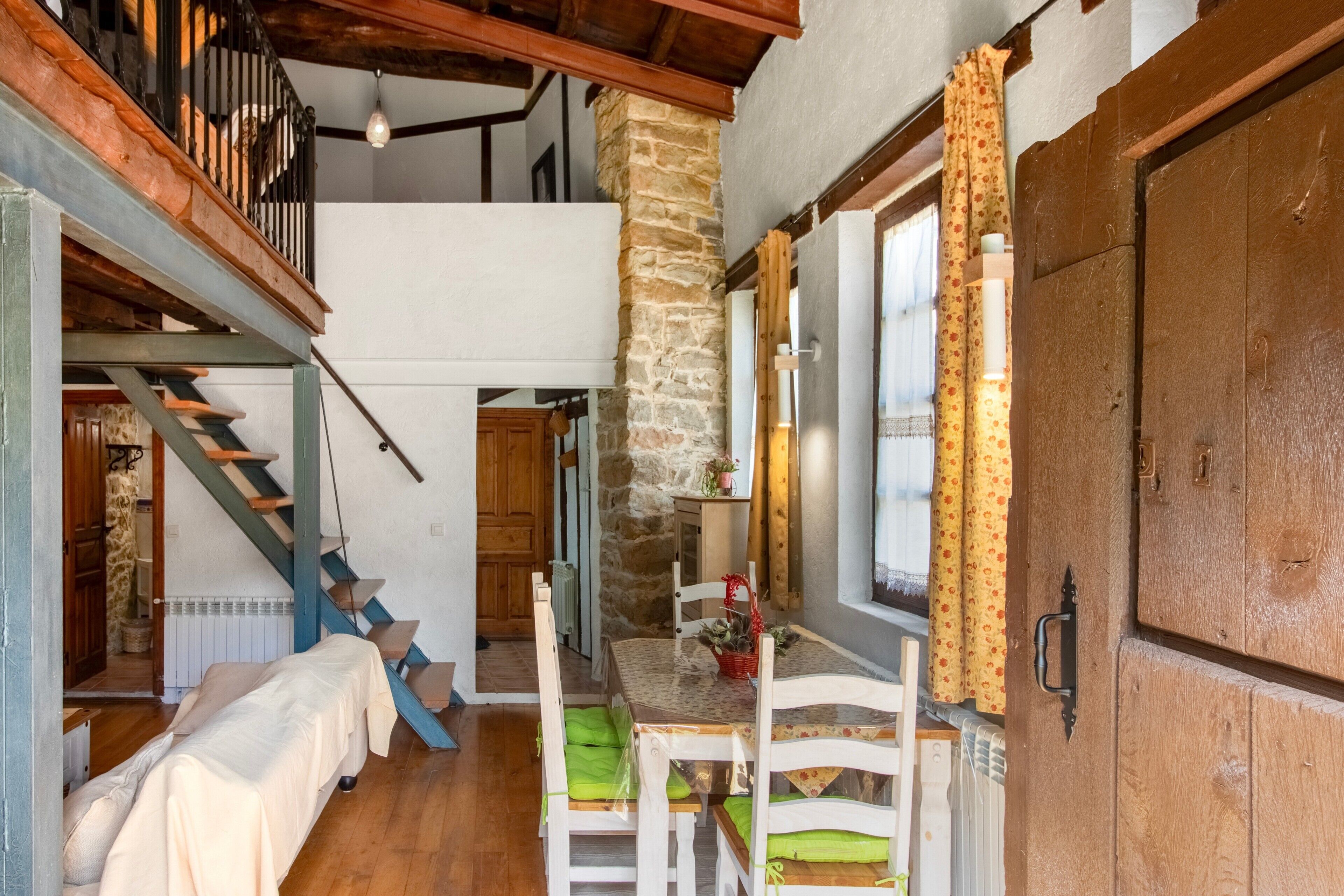 A cozy room with a wooden staircase, a dining area with a table and chairs, and a large wooden door.