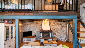 Uma sala de estar aconchegante com lareira de pedra, televisão e escada de madeira.