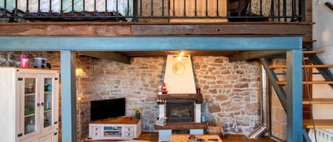 Una sala de estar acogedora con chimenea de piedra, televisor y escalera de madera.