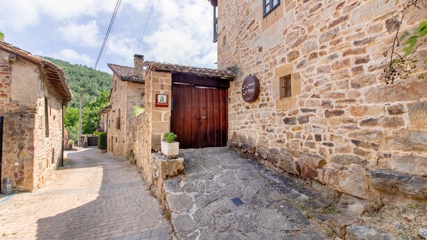 Uma rua de pedra estreita com um edifício rústico, uma porta de madeira e uma placa.