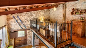Interior rústico de pedra com escada de madeira, guarda-corpo de metal e parede de pedra.