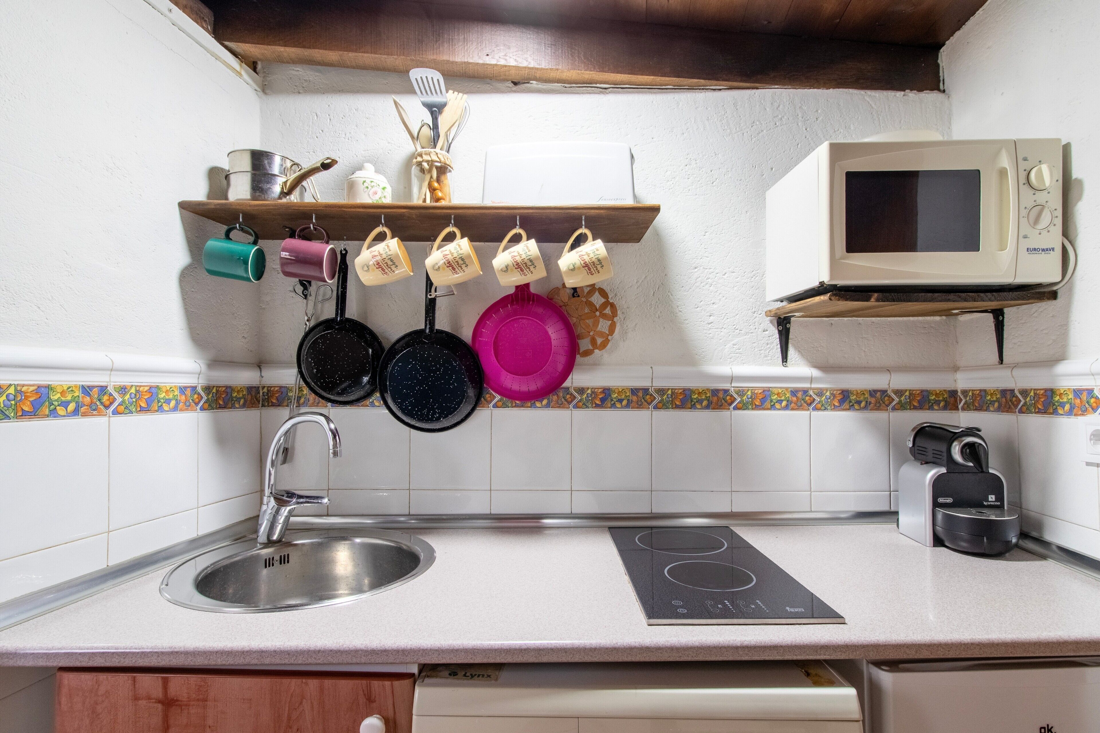 Une cuisine équipée d’un évier, d’une cuisinière, d’un four à micro-ondes et d’une étagère où sont rangés les ustensiles et les tasses.
