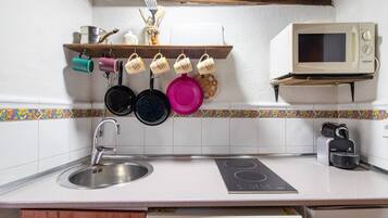 Une cuisine équipée d’un évier, d’une cuisinière, d’un four à micro-ondes et d’une étagère où sont rangés les ustensiles et les tasses.