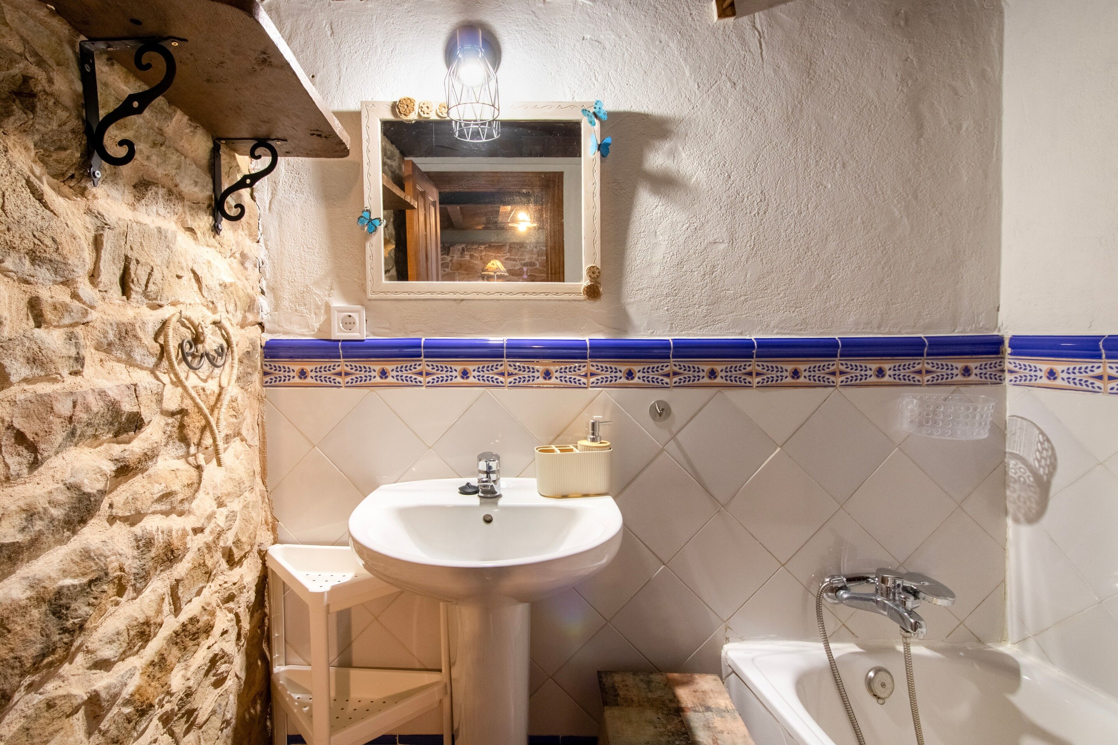 Une salle de bain avec un mur en pierre, un lavabo, un miroir et une baignoire.