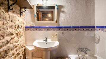 Une salle de bain avec un mur en pierre, un lavabo, un miroir et une baignoire.