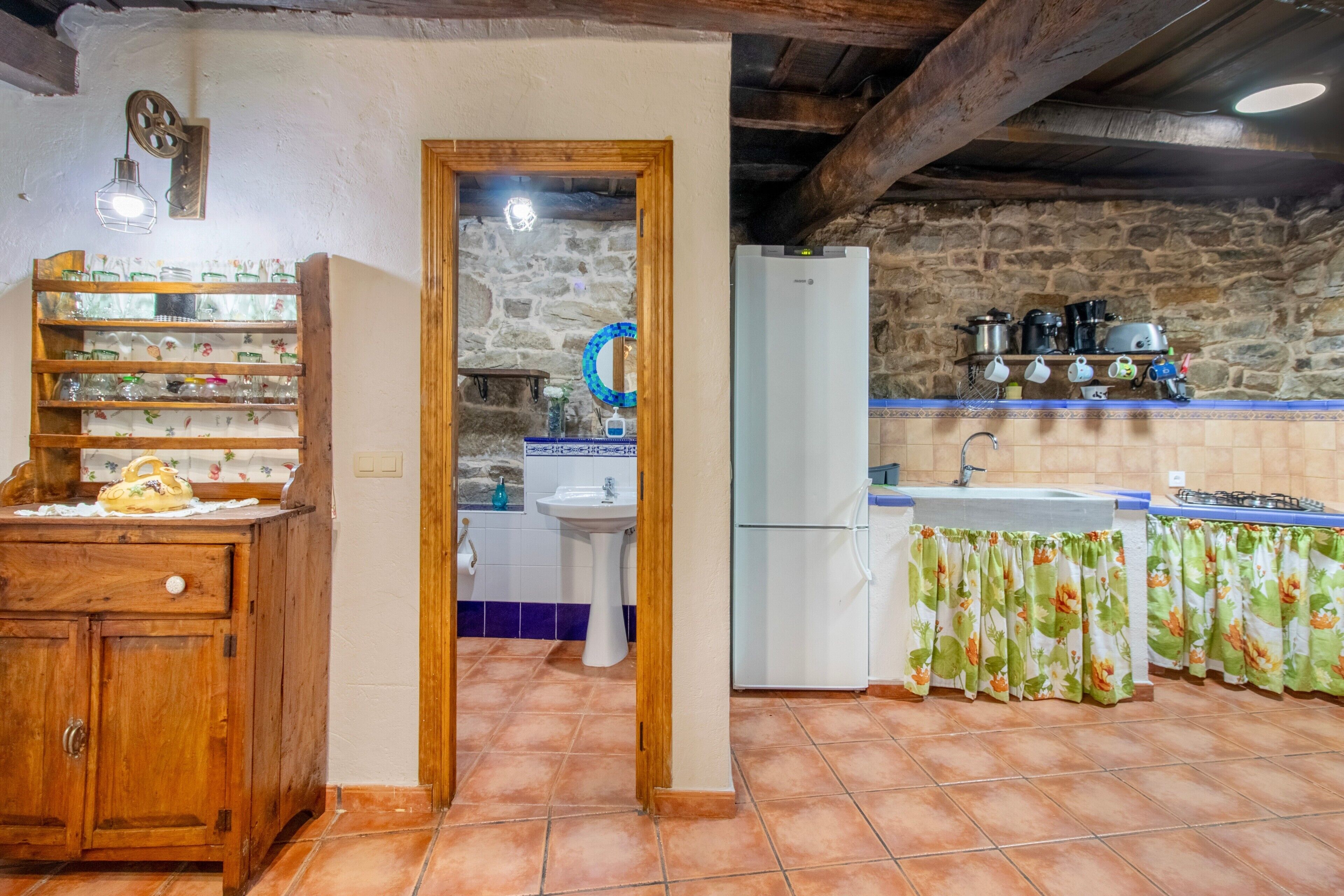 Una cocina rústica con un armario de madera, un fregadero, un refrigerador y una pared de piedra.