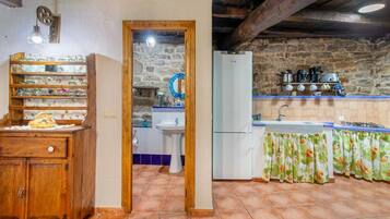Una cocina rústica con un armario de madera, un fregadero, un refrigerador y una pared de piedra.