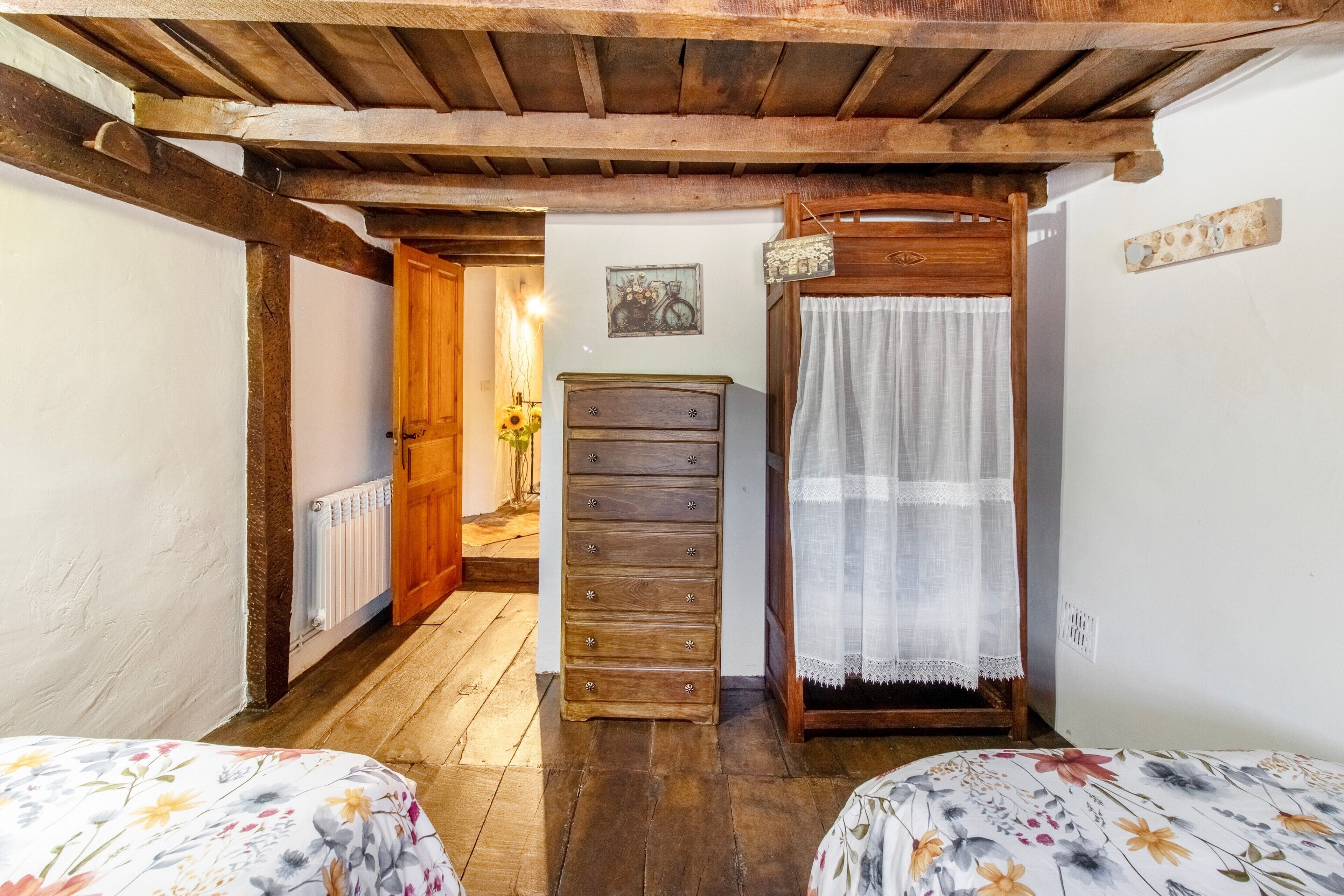 Un dormitorio con vigas de madera, un aparador de madera, una cama con ropa de cama floral y una mesita de noche con lámpara.