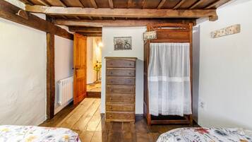 Un dormitorio con vigas de madera, un aparador de madera, una cama con ropa de cama floral y una mesita de noche con lámpara.