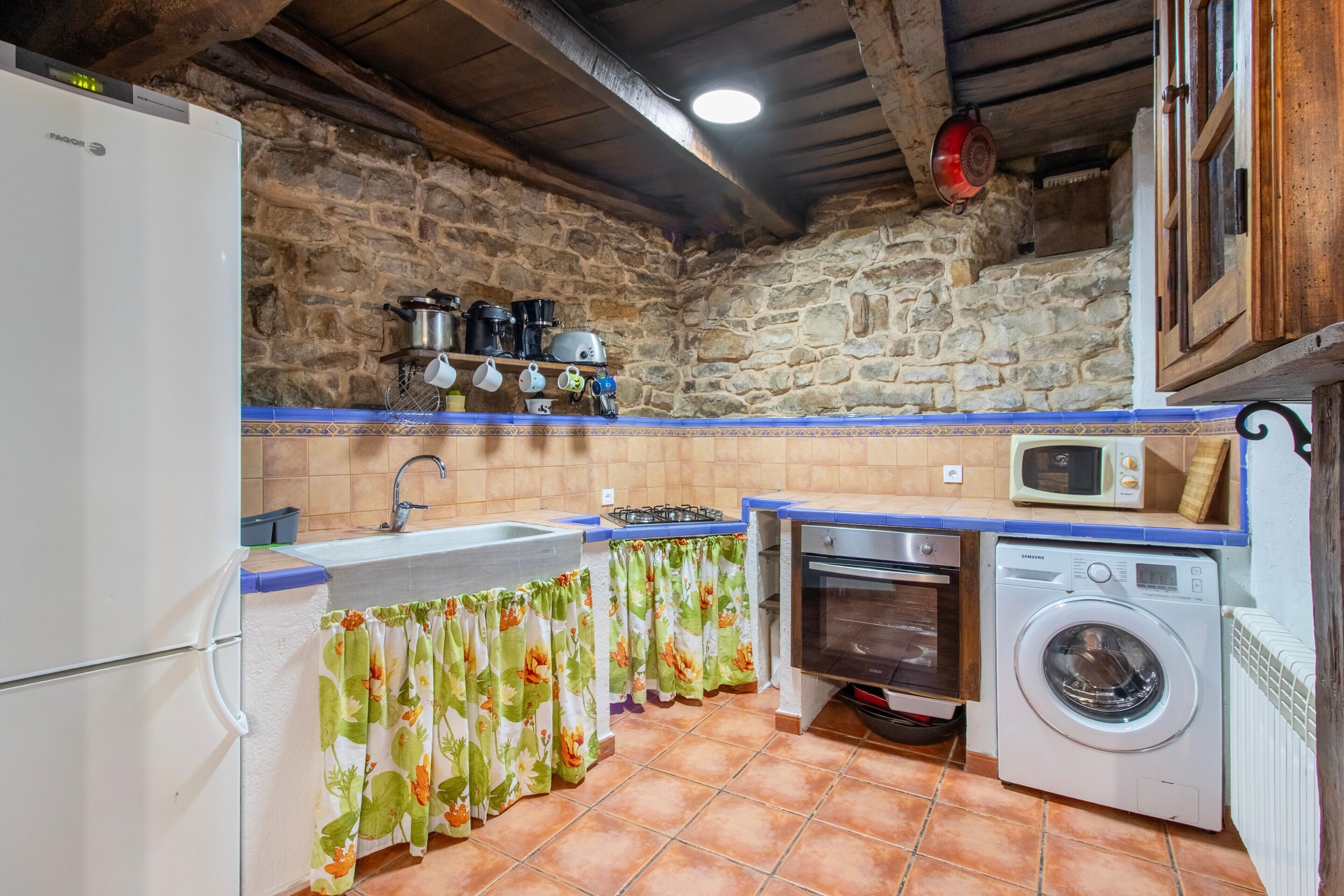Una cocina con pared de piedra, lavadora, horno y microondas.